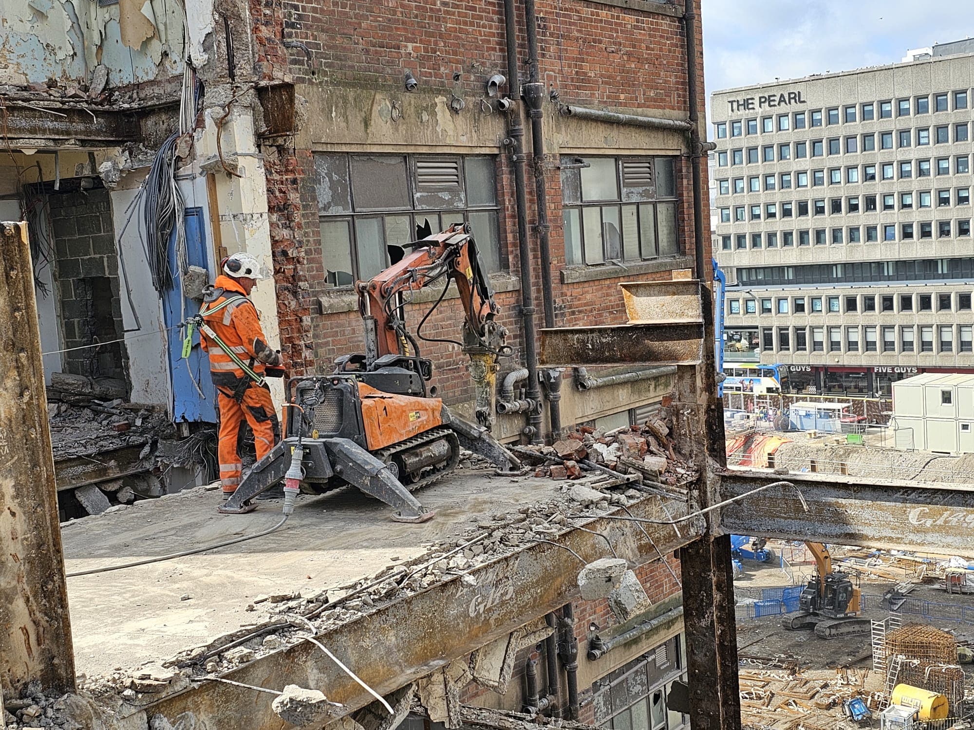 GNAT UK operator and orange Brokk pecker working from the cleared top floor of a listed brick building, with "The Pearl" listed structure visible across the cleared site
