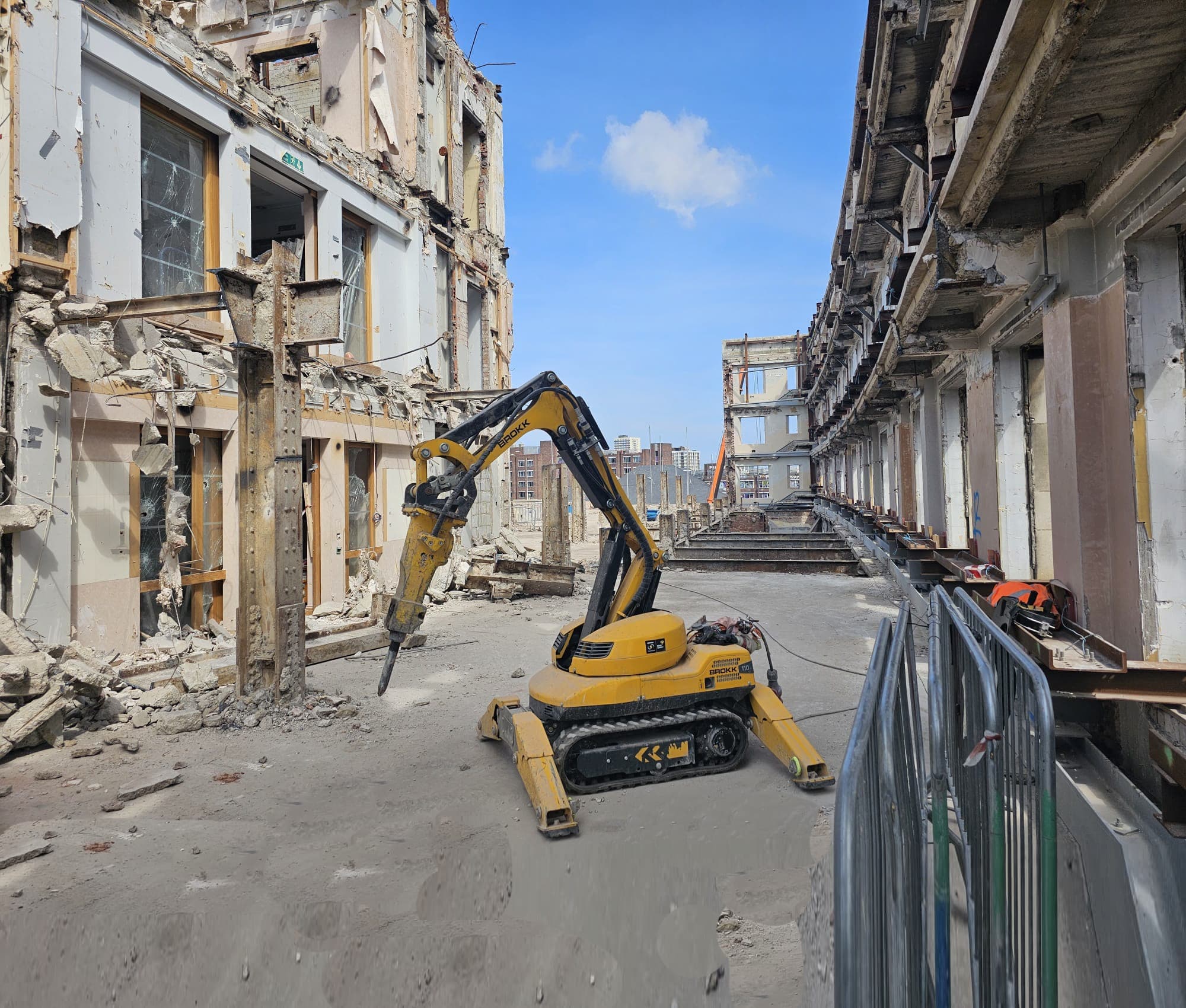 Wide view of a heritage facade-retention scheme — the listed elevation propped in place while a Brokk robot deconstructs the internal floors and structure behind it