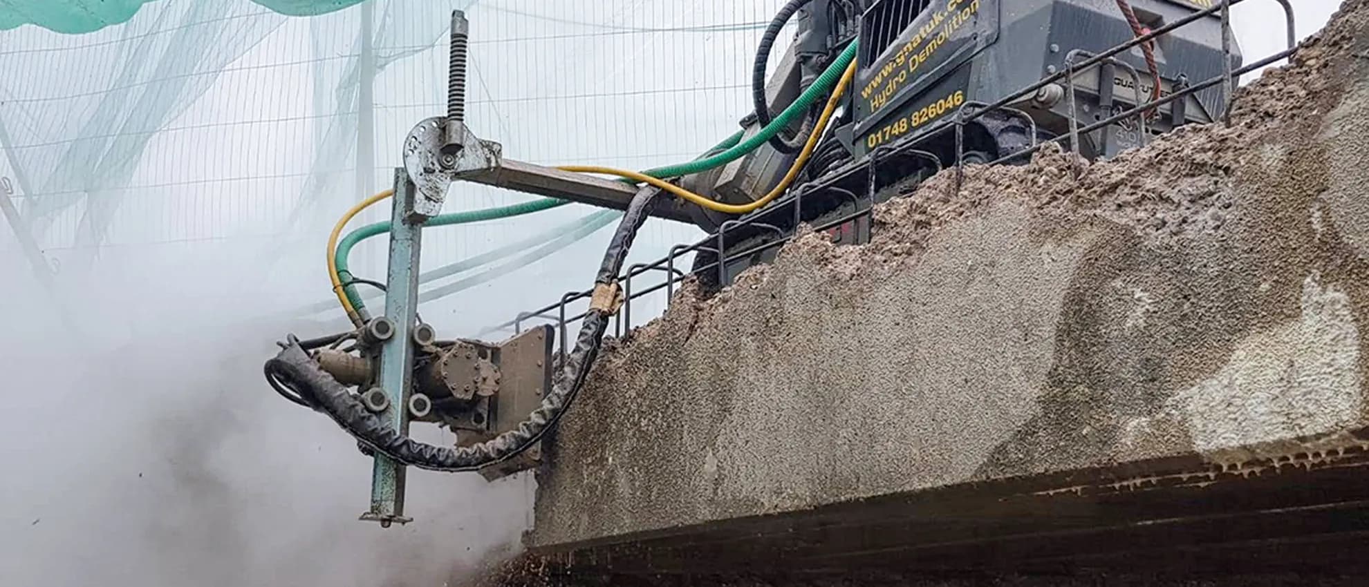 GNAT-branded Aquajet hydrodemolition robot performing selective concrete removal on a motorway bridge parapet — water management and live-carriageway-adjacent working