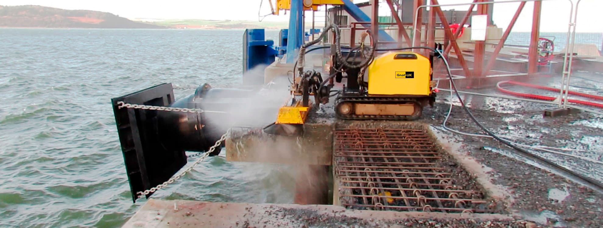 Aquajet hydrodemolition rig with GNAT UK branding mobilised on a North Sea coastal jetty, selectively removing deteriorated marine concrete while preserving the rebar