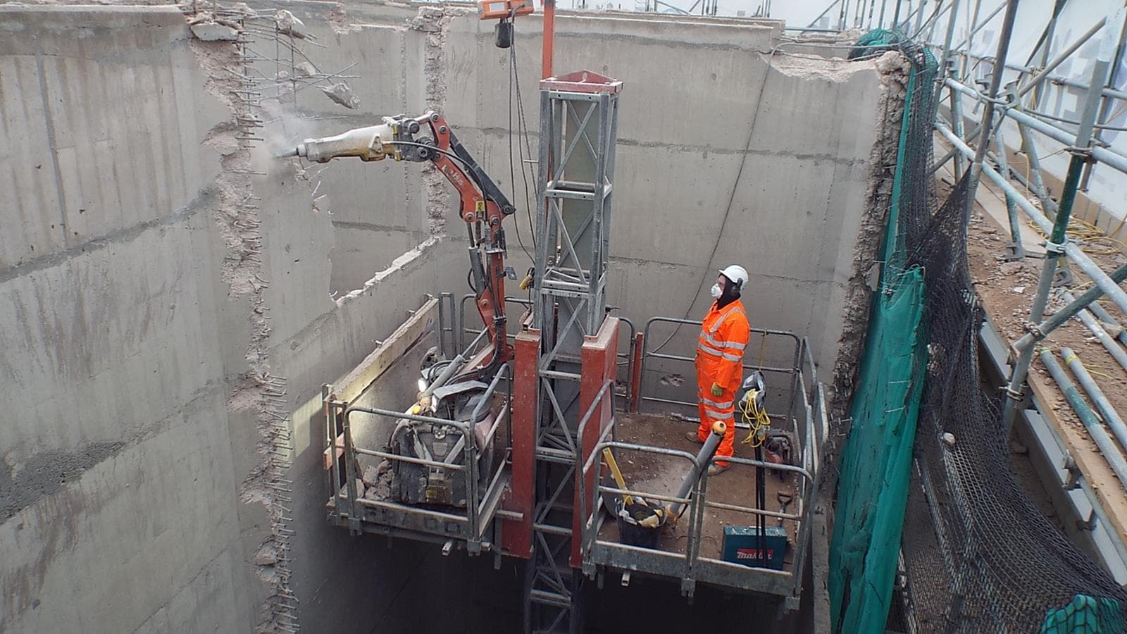 GNAT UK operator and Brokk pecker working from a confined-access platform inside a deep coastal excavation — selective concrete removal against an in-service marine asset