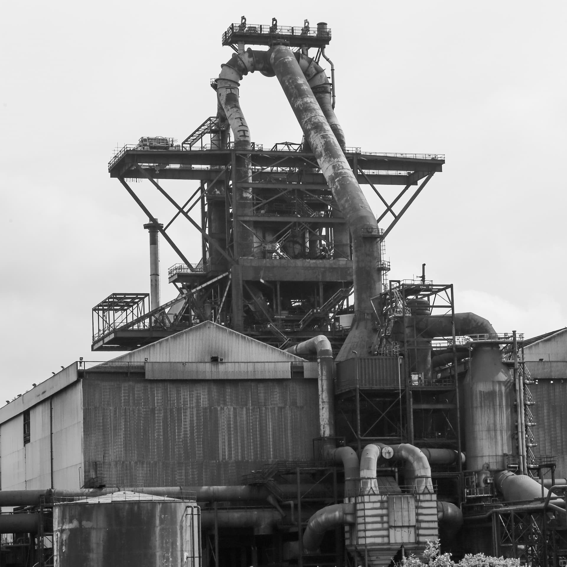 Close-up black-and-white study of a British Steel blast-furnace head — the structural scale and pipework complexity of UK heavy-industrial process equipment