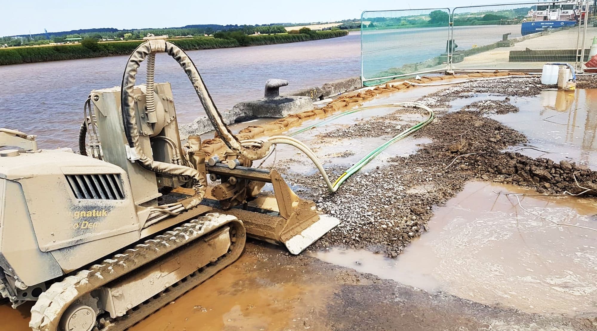 GNAT UK robotic plant on a riverside water-industry dock — selective demolition and removal works on an asset being brought back into service, water management hose running into the channel alongside
